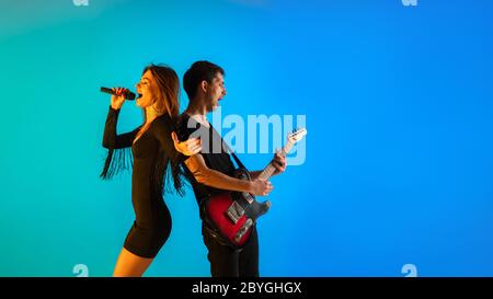 Kaukasische Musiker, Sänger und Gitarrist, isoliert auf blauem Studiohintergrund in Neonlicht. Inspiriert improvisieren, performt. Konzept der menschlichen Emotionen, Gesichtsausdruck, Werbung, Musik, Kunst, Festival. Stockfoto