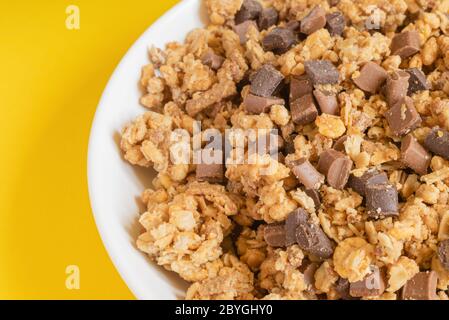 Müsli knusprig muesly mit Stücken von dunkler und Milchschokolade in einer Schüssel auf hellgelbem Hintergrund. Müsli mit Rückendeckung. Draufsicht. Makro. Speicherplatz kopieren. Stockfoto