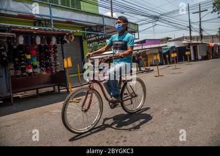 San Pedro Sula, Honduras. Mai 2020. Ein Mann, der vorbeugend eine Gesichtsmaske trägt, fährt mit dem Fahrrad durch einen verlassenen Marktplatz. Honduras hat eine "intelligente Wiedereröffnung" ins Land gebracht, die es allen kommerziellen Unternehmen ermöglichte, sich zu öffnen, aber alle Angestellten und Kunden dazu aufforderte, Masken zu tragen. Quelle: SOPA Images Limited/Alamy Live News Stockfoto