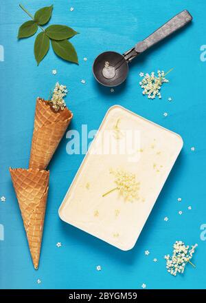 Hausgemachtes Holunderblüteneis in einer kleinen Metallform mit Waffelkegel und rustikalem Schaufelbecher. Draufsicht. Stockfoto