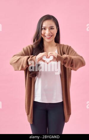 Asiatische Frau macht eine Herzform mit ihren Händen, isoliert über rosa Hintergrund Stockfoto