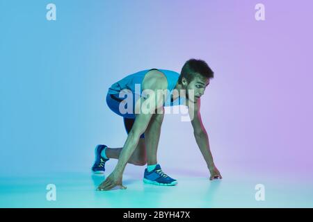 Porträt von aktiven jungen kaukasischen Mann Laufen, Joggen auf Gradienten Studio Hintergrund in Neonlicht. Profi-Sportler trainieren in Aktion und Bewegung. Sport, Wellness, Aktivität, Vitalität Konzept. Stockfoto