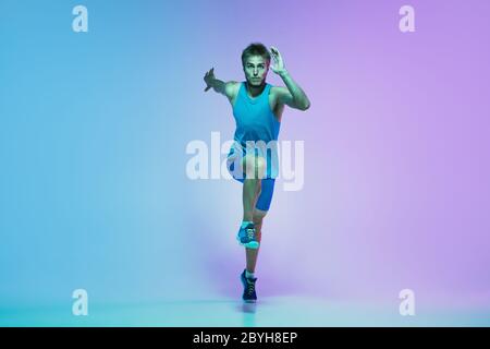 Porträt von aktiven jungen kaukasischen Mann Laufen, Joggen auf Gradienten Studio Hintergrund in Neonlicht. Profi-Sportler trainieren in Aktion und Bewegung. Sport, Wellness, Aktivität, Vitalität Konzept. Stockfoto