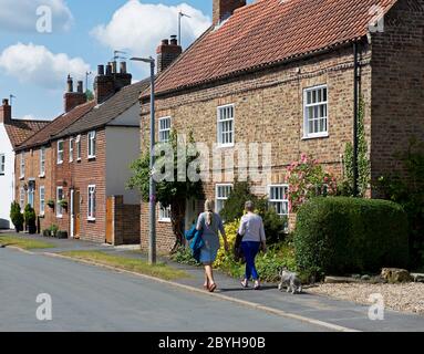 Zwei Frauen, die entlang der Hauptstraße von Shittonthorpe, einem Dorf in East Yorkshire, England, spazieren Stockfoto