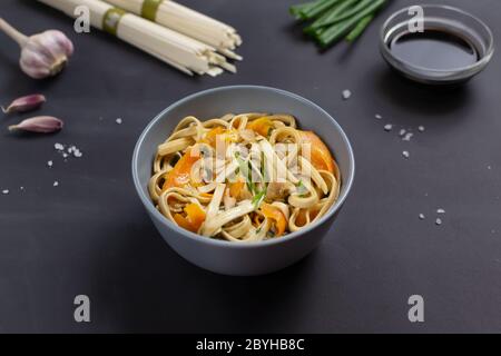 Udon-Nudeln mit Huhn, Sojasauce, Bambusstäbchen und frischen Zutaten auf schwarzem Hintergrund. Japanische Küche. Stockfoto