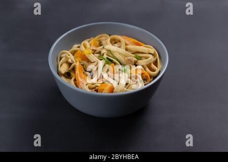 Udon Nudeln mit Huhn in einer grauen Schüssel auf schwarzem Hintergrund. Nahaufnahme. Minimalismus. Japanische Küche. Stockfoto