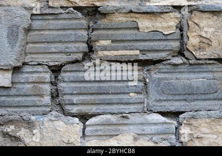 Die Textur der Wand mit den abfallenden keramischen Fliesen. Die Außenwand des Gebäudes mit Zementmörtel. Schlechter Auftragnehmer. Bauindustrie Stockfoto