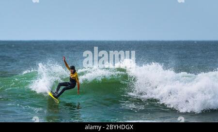Ein Panoramabild eines jungen Surfers, der eine Welle bei Fistral in Newquay in Cornwall reitet. Stockfoto