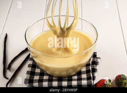 Pfannkuchen oder Kuchen, Bäcker Hände Gießen Teig und Whisking Teig in Schüssel. Konzept der Zutaten und Methode auf weißem Holzhintergrund, Stockfoto