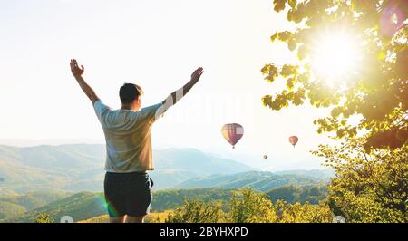 Abenteuerlicher Mann steht auf einem Berg und genießt eine schöne Aussicht während viele Ballons. Das aktive Lifestyle-Wochenende. Luftballons fliegen Stockfoto