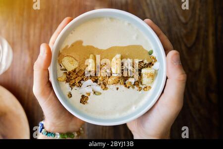 Essen Frühstücksschale. Joghurt, Erdbeere, Heidelbeere, Samen, Kokosnuss, frische und trockene Früchte in weiß Keramik Schüssel in den Händen. Sauberes Essen, Diät Stockfoto