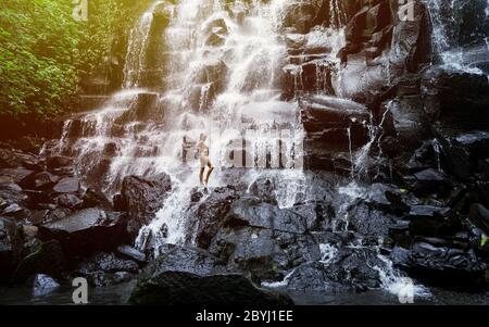 Erstaunliche Frau genießen unter Strom von großen und schönen Wasserfall. Mädchen mit schlanken Körper und lange schwarze Haare. Kanto Lampo im Gebiet Ubud, Stockfoto