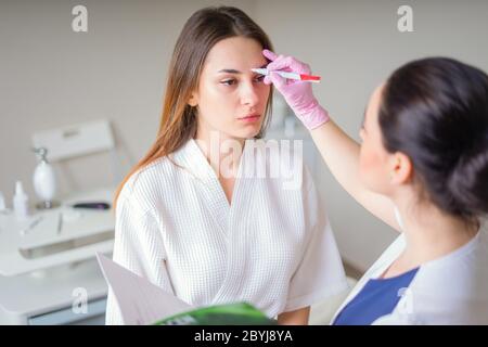 Kosmetologe bereit, Linien mit Marker auf dem Gesicht des Patienten zu malen Stockfoto