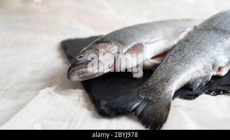 Zwei Regenbogenforellen auf einem schwarzen Steinbrett. Fisch für Suppe vorbereitet. Fisch Suppe Zutat. Ausschneiden der Fische Stockfoto