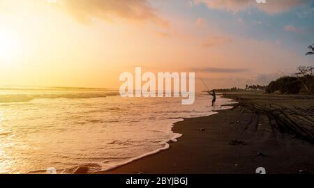 Silhouette eines Fischers beim wunderschönen Sonnenuntergang Sonnenaufgang und Wellen auf dem Canggu Jimbaran Sanur Strand, Bali Indonesien Stockfoto