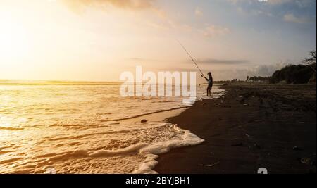 Silhouette eines Fischers beim wunderschönen Sonnenuntergang Sonnenaufgang und Wellen auf dem Canggu Jimbaran Sanur Strand, Bali Indonesien Stockfoto