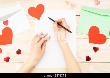 Girl's Hand schreibt einen Liebesbrief. Valentinstag. Handgefertigte Grußkarte mit einem roten Herz in Form einer Figur. Der 14. Februar ist ein Fest der Stockfoto