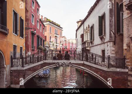 Zwei Liebhaber sitzen Seite an Seite auf einer Brücke über einen Kanal zwischen rosa Gebäuden in Venedig, Italien Stockfoto