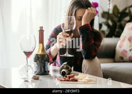 Traurige müde Frau, Wein zu Hause trinken, allein, auf dem Boden im Wohnzimmer sitzen, Gefühl depressiv Stockfoto