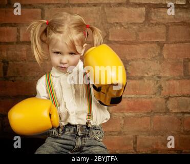 Kleines Mädchen mit gelben Boxhandschuhen über der Ziegelwand Stockfoto