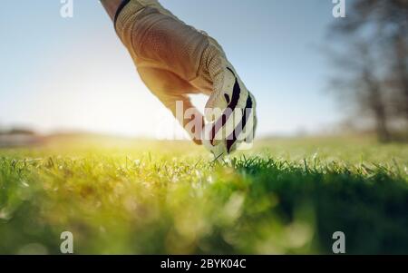 Hand Putting Golfball auf Tee im Golfplatz bei Sonnenuntergang, Sonnenaufgang Zeit. Golf-Konzept Stockfoto