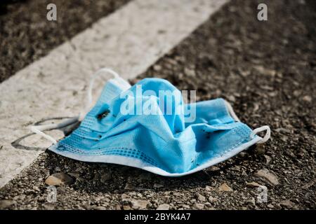 Nahaufnahme einer blauen chirurgischen Maske auf dem Asphalt einer Straße, eines Parkplatzes oder einer Straße geworfen Stockfoto