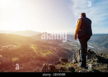 Glücklicher alter Mann erreicht gerade die Spitze des Hügels. Schöner Senior auf der Bergspitze vor dem Hintergrund des Sonnenuntergangs. Tal beobachten Sonnenuntergang in den letzten Sonnenstrahlen. Stockfoto
