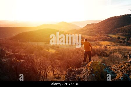 Glücklicher alter Mann erreicht gerade die Spitze des Hügels. Schöner Senior auf der Bergspitze vor dem Hintergrund des Sonnenuntergangs. Tal beobachten Sonnenuntergang in den letzten Sonnenstrahlen. Stockfoto