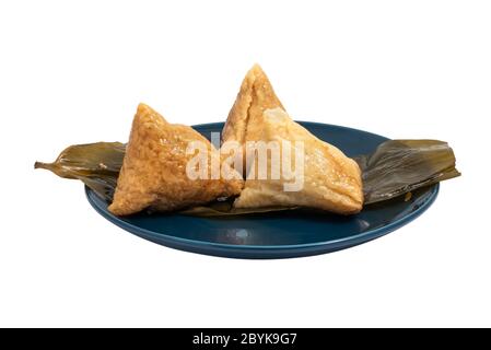 Three opened ZhongZi - traditionelle chinesische Reisgericht in Bambusblättern auf einem blauen Teller isoliert auf weiß Stockfoto