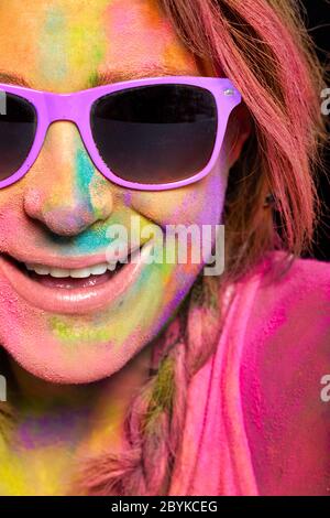 Schöne junge Frau in Regenbogen farbigen Holi Pulver bedeckt. Nahaufnahme fröhliche Modell Mädchen in bunten Sonnenbrillen und Gesicht mit bunten Pulver bedeckt Stockfoto