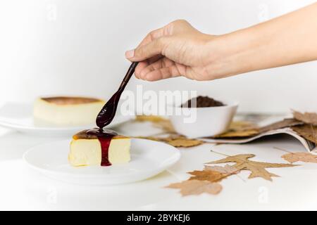 Frau gießt Beeren-Sauce auf Scheibe baskischen gebrannten Käsekuchen. Stockfoto