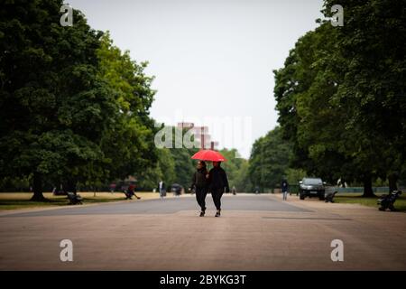 Mitglieder der öffentlichen Schutzhütte vor dem Regen unter einem Regenschirm in Kensington Gardens, da Großbritannien voraussichtlich am Wochenende mit starken Regenschauern, starken Stürmen und kälteren Temperaturen getroffen werden wird, wobei die Briten gewarnt werden, Versammlungen nicht in Innenräumen zu verlegen. Stockfoto