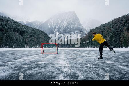 Eishockeyspieler schießt und schießt. Spieler auf einem gefrorenen Teich. Schlittschuhe auf den Füßen des Spielers während des Eishockeys. Eishockeyspieler, der auf einem gefrorenen Teich trainiert Stockfoto