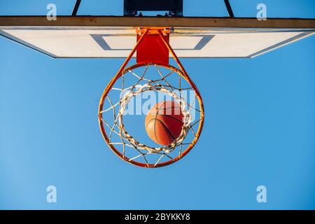 Street Basketball Ball fallen in den Reifen. Urban Jugend Spiel. Nahaufnahme der orangefarbenen Kugel über dem Netz. Konzept des Erfolgs, Punkte sammeln und gewinnen Stockfoto