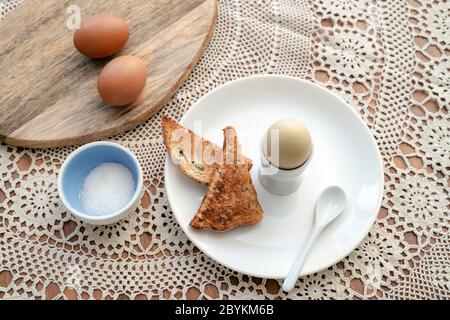 Leckeres gekochtes Ei in einer Tasse mit knusprig geröstetem Brot zum Frühstück. Gesundes Essen auf dem Küchentisch. Stockfoto