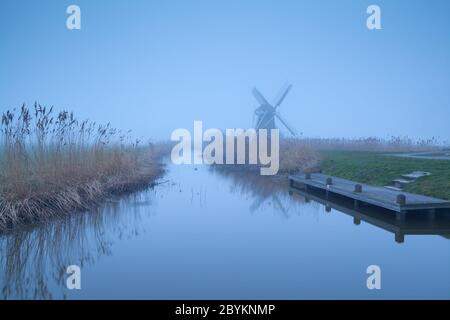 Holländische Windmühle im dichten Nebel durch Fluss Stockfoto