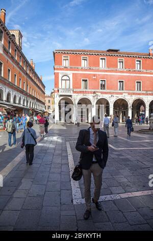 Geschäftsmann, der über Campo San Giacomo di Rialto, Venedig, Italien läuft, während er sein Mobiltelefon mit Gebäuden im Hintergrund völlig absorbiert Stockfoto