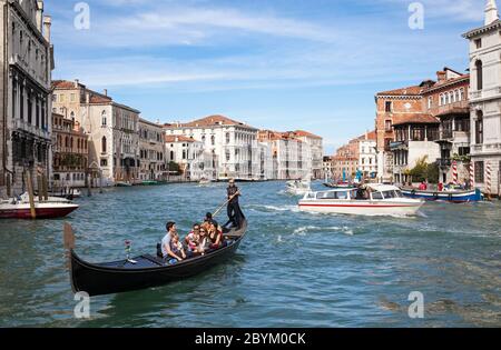 Familie mit einem kleinen Baby bei einer Gondelfahrt auf einem abgehackten Canal Grande in Venedig, Italien, sonnenbeschienene Gebäude im Hintergrund unter blauem Himmel Stockfoto