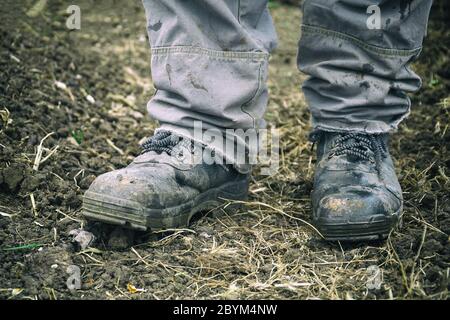 Füße des Arbeiters in staubigen Stiefeln. Ein Mann in Overalls und Arbeitsstiefeln. Arbeitskleidung Stockfoto