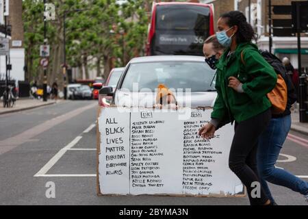 Ein Mädchen, das auf einer Straße sitzt und ein Schild den Verkehr während eines Black Lives Matters Protests blockiert, London, 7. Juni 2020 Stockfoto