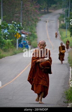 Buddhistische Mönche, die zu Fuß oder in ein Dorf transportiert werden, um Lebensmittelspenden zu sammeln. Stockfoto