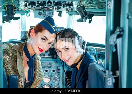Zwei Frauen Piloten sitzen in der Kabine der modernen Flugzeuge. Lächelnde Stewardess im Flugzeug. Porträt einer attraktiven Frau Trainee Pilot mit Headset-Vorbereitung Stockfoto