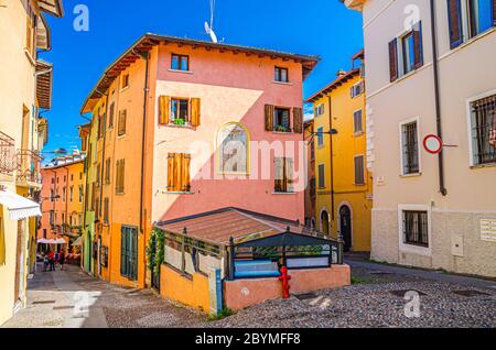 Desenzano del Garda, Italien, 11. September 2019: Typische schmale Straße in der Altstadt mit Kopfsteinpflasterstraße und traditionellen bunten Gebäuden, blauer Himmel Hintergrund, Lombardei Stockfoto