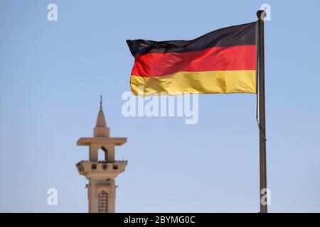 27.02.2020, Doha, , Katar - Nationalflagge der Bundesrepublik Deutschland winkt vor einem Minarett. 00S200227D372CAROEX.JPG [MODELLFREIGABE: NEIN, Stockfoto