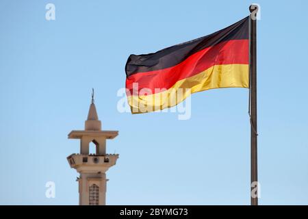 27.02.2020, Doha, , Katar - Nationalflagge der Bundesrepublik Deutschland winkt vor einem Minarett. 00S200227D371CAROEX.JPG [MODELLFREIGABE: NEIN, Stockfoto