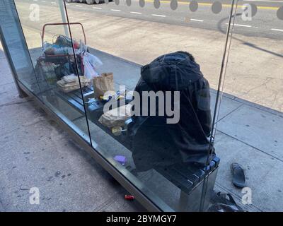 Obdachloser, der seinen Wohnraum an einer Bushaltestelle in Brooklyn, New York, eingerichtet hat. Stockfoto