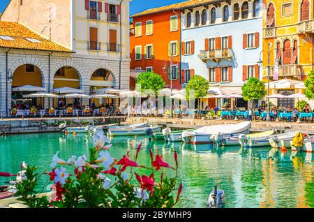 Desenzano del Garda, Italien, 11. September 2019: Alter Hafen Porto Vecchio mit Booten auf türkisfarbenem Wasser, Straßenrestaurants und traditionellen Gebäuden im historischen Stadtzentrum, Lombardei Stockfoto