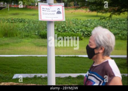 15.05.2020, Singapore, , Singapur - EINE Frau mit Mundschutz geht an einem Covid-19 Schild im Bishan-Ang Mo Kio Park vorbei, das auf obligatorische Meas hinweist Stockfoto