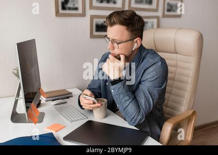 Junger, ernsthafter, schöner weißer Mann, der mit Kopfhörern von zu Hause aus an einem Laptop arbeitet. Stockfoto