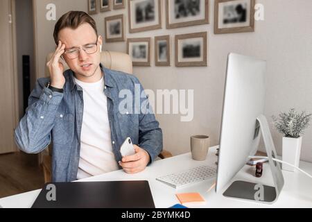 Junger, ernsthafter, schöner weißer Mann, der mit Kopfhörern von zu Hause aus an einem Laptop arbeitet. Stockfoto